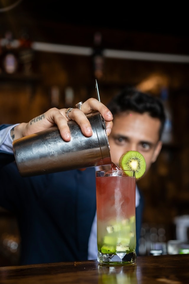 Action shot of a bartender pouring a kiwi cocktail with moody, editorial lighting