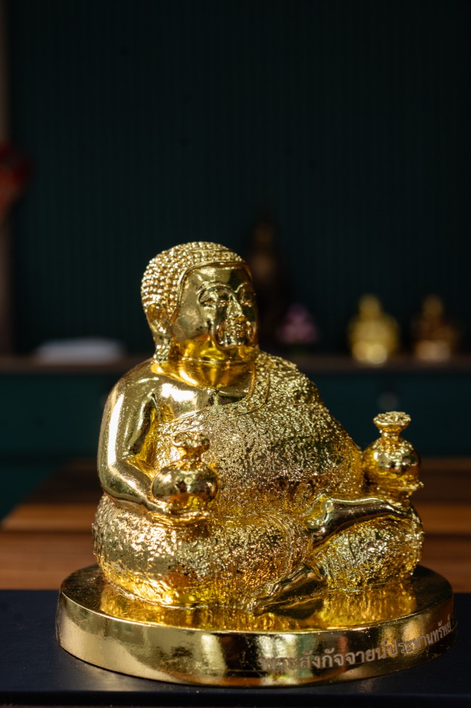 Close-up product detail photo of a golden Buddha figure with moody, minimal lighting